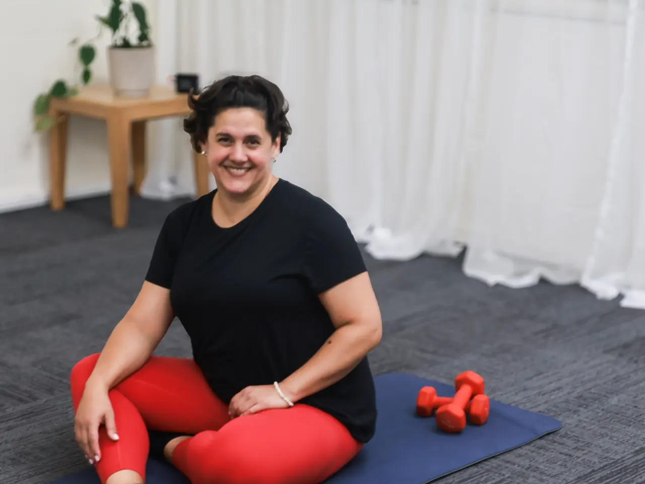 Seated on a Pilates mat with red dumbbells, group mat class Pilates Wollongong